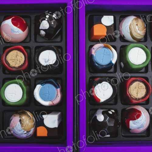 High angle close up of selection of bonbons in a purple and black box. High angle close up of selection of bonbons in a purple and black box.