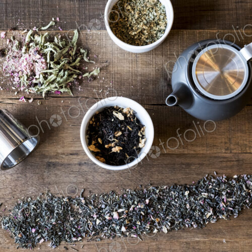 High angle close up of selection of tea leaf infusions and black teapot on wooden table.