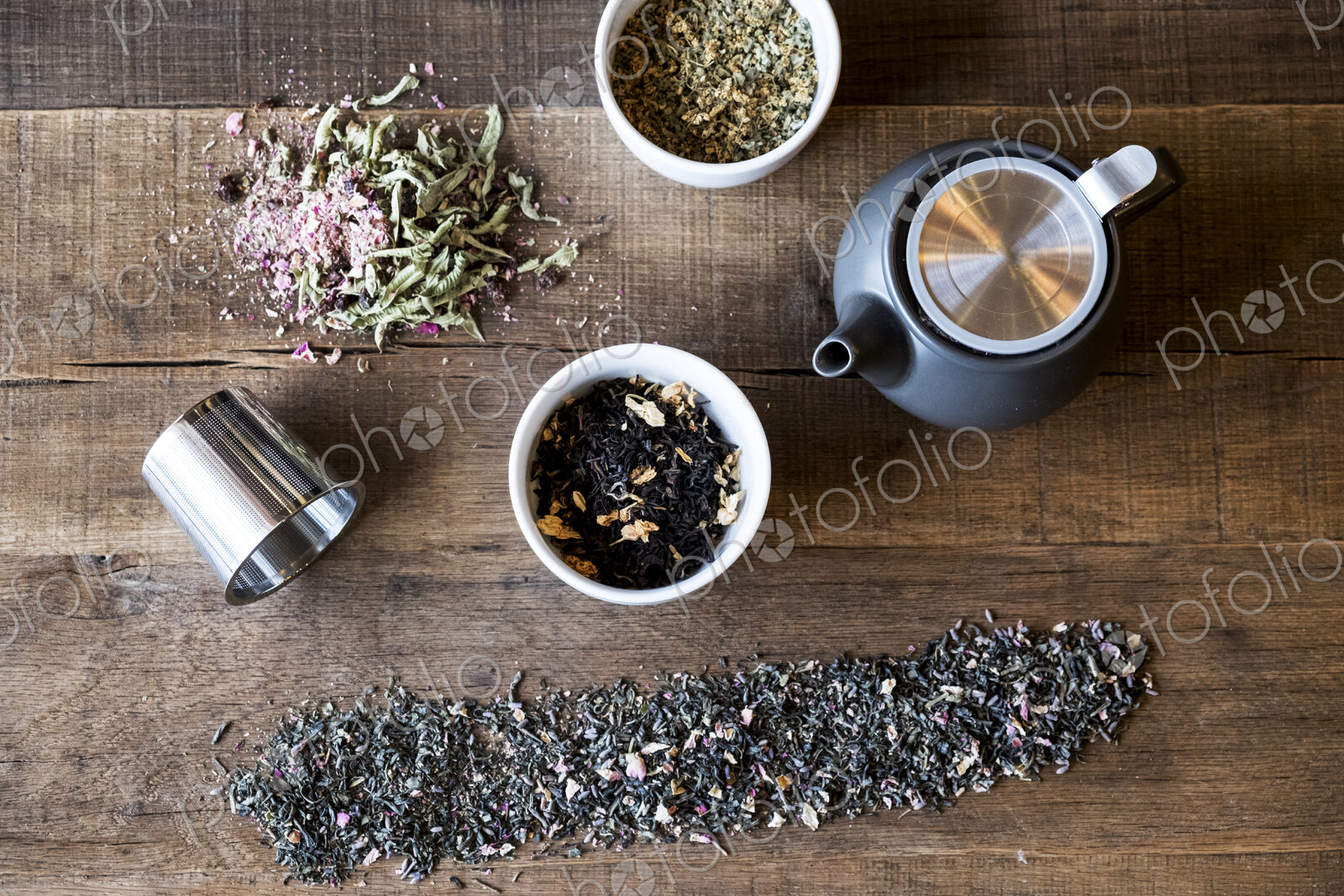 High angle close up of selection of tea leaf infusions and black teapot on wooden table.