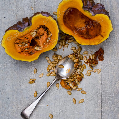 High angle close up of silver tablespoon and purple pumpkin with orange flesh cut in half.