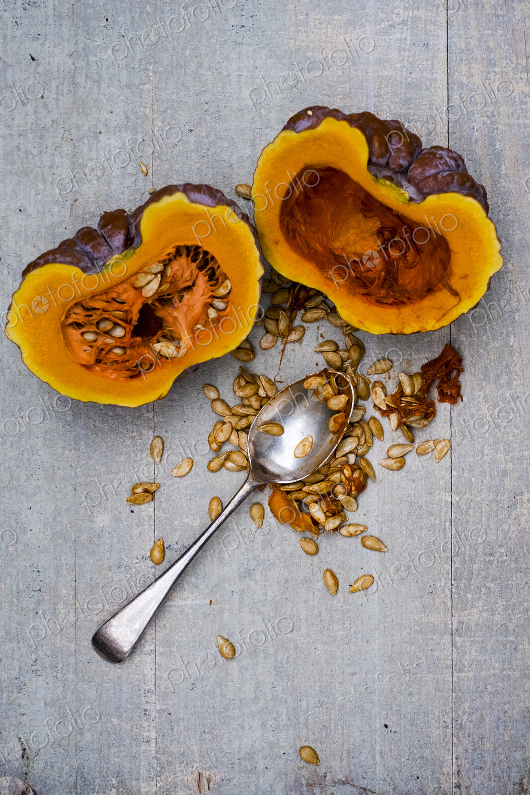High angle close up of silver tablespoon and purple pumpkin with orange flesh cut in half.
