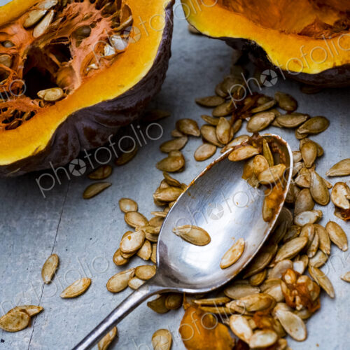 High angle close up of silver tablespoon and purple pumpkin with orange flesh cut in half.