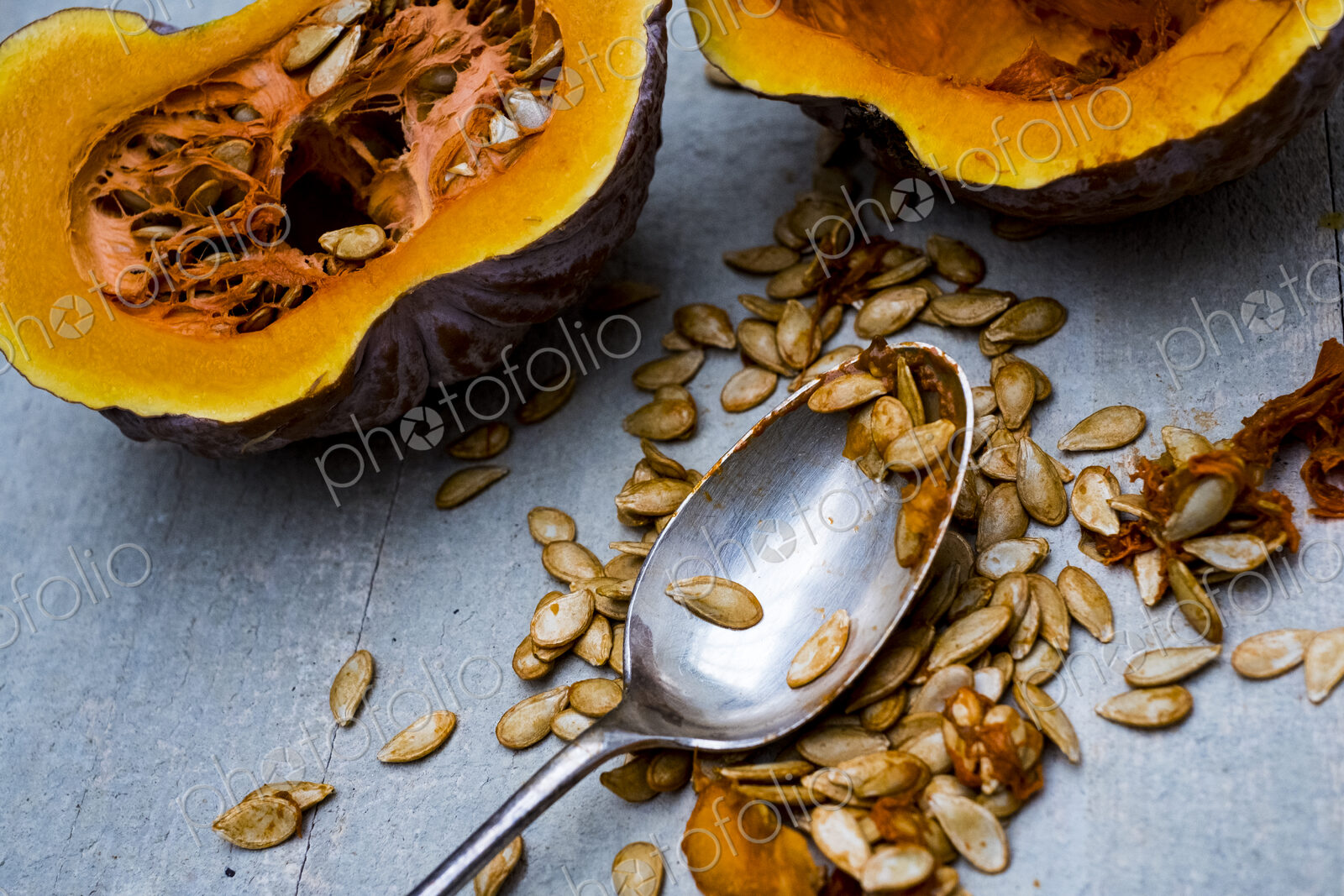 High angle close up of silver tablespoon and purple pumpkin with orange flesh cut in half.