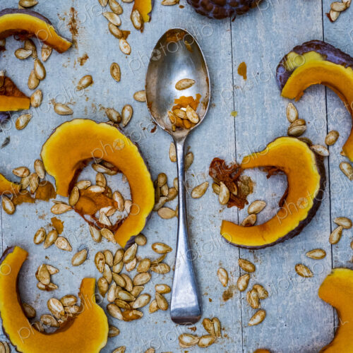 High angle close up of silver tablespoon and slices of pumpkin on blue background.