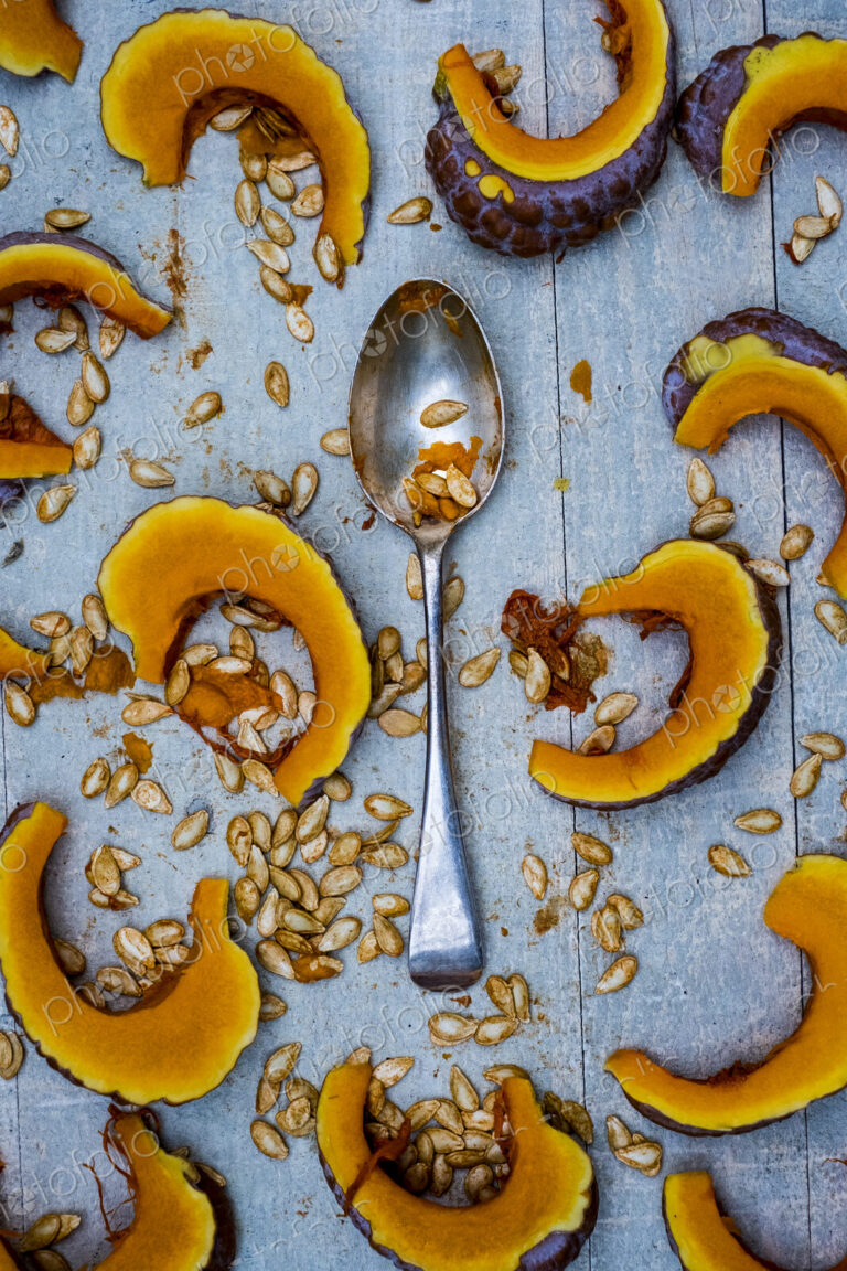 High angle close up of silver tablespoon and slices of pumpkin on blue background.