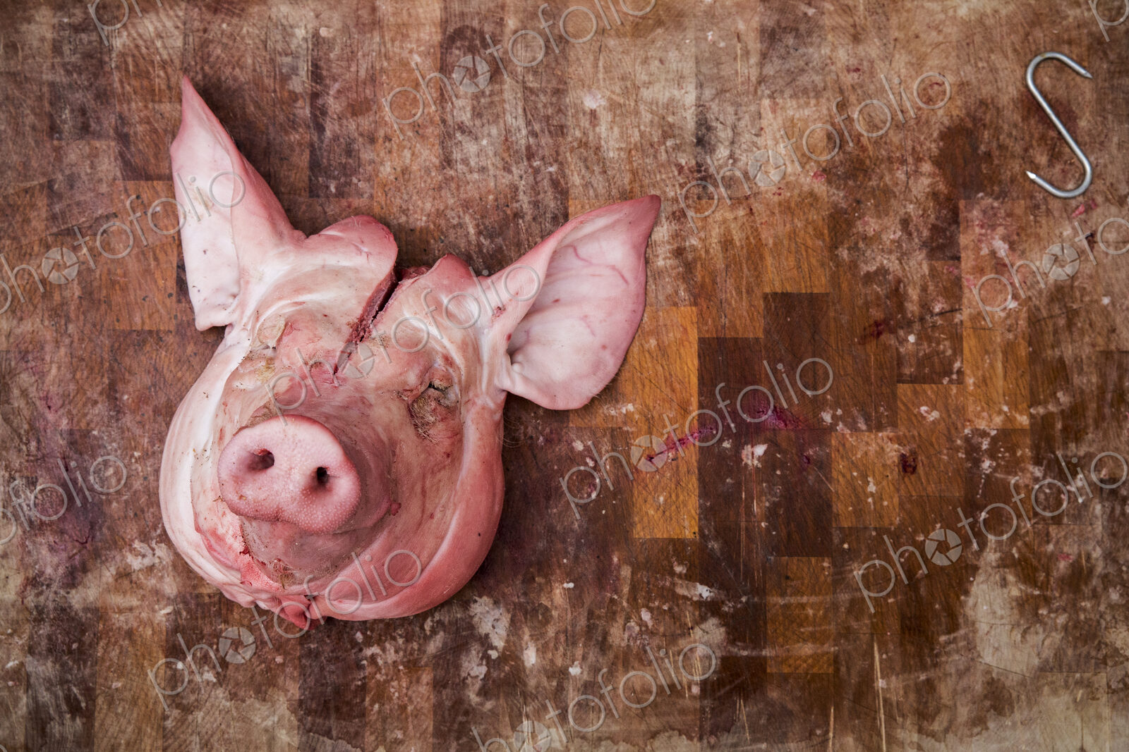 High angle close up of slaughtered pig’s head on wooden butcher’s block.