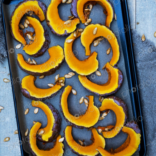 High angle close up of slices of pumpkin on a baking tray. High angle close up of slices of pumpkin on a baking tray.