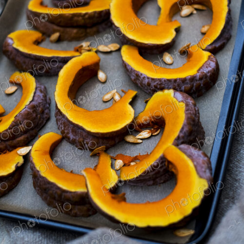 High angle close up of slices of pumpkin on a baking tray. High angle close up of slices of pumpkin on a baking tray.