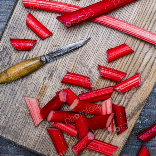 High angle close up of slices of rhubarb and knife on wooden cutting board. High angle close up of slices of rhubarb and knife on wooden cutting board.