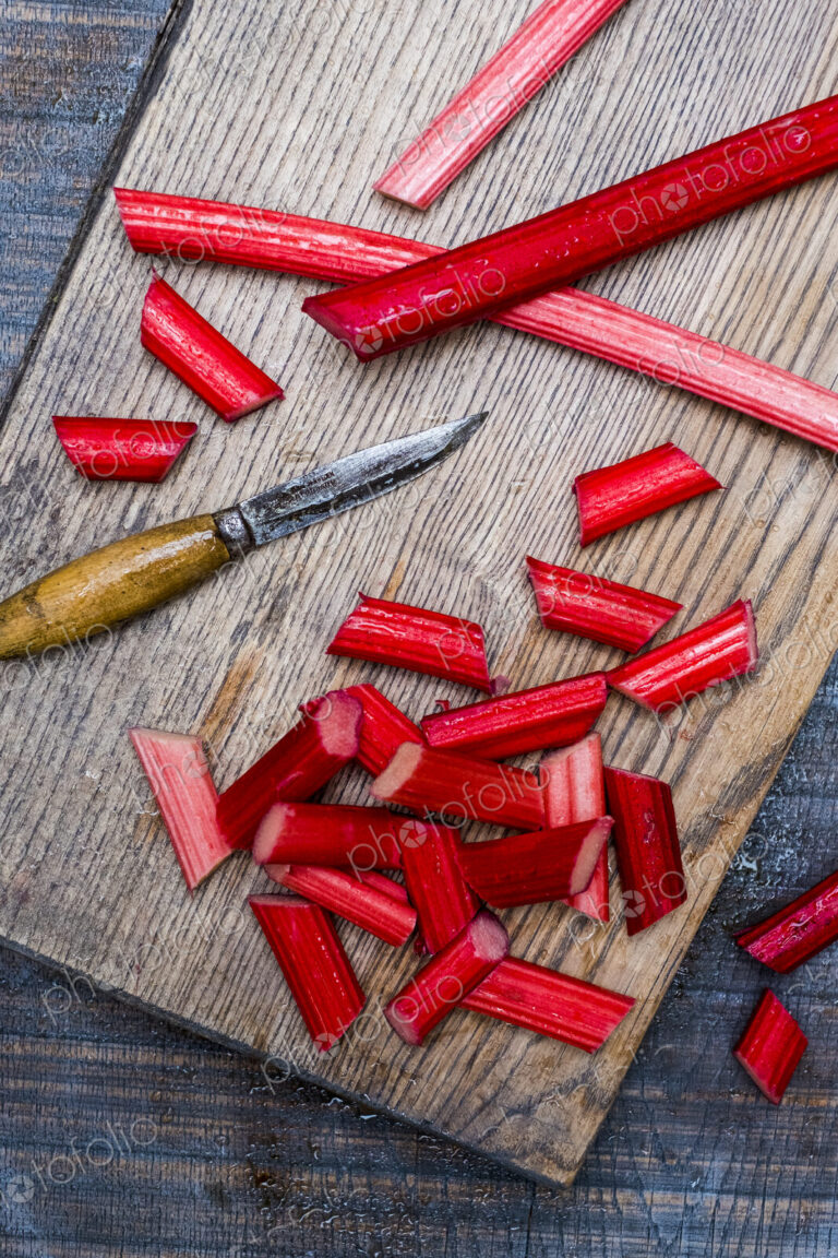 High angle close up of slices of rhubarb and knife on wooden cutting board.
