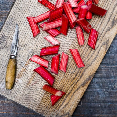 High angle close up of slices of rhubarb and knife on wooden cutting board. High angle close up of slices of rhubarb and knife on wooden cutting board.