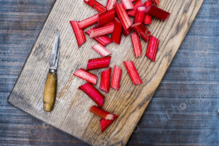 High angle close up of slices of rhubarb and knife on wooden cutting board.