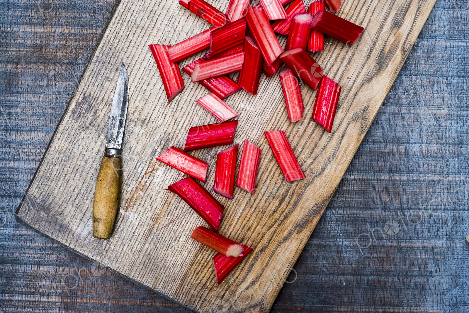 High angle close up of slices of rhubarb and knife on wooden cutting board.