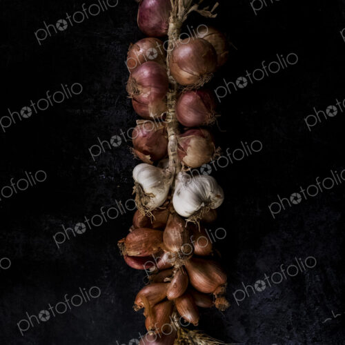 High angle close up of string of onions and garlic on black background. High angle close up of string of onions and garlic on black background.