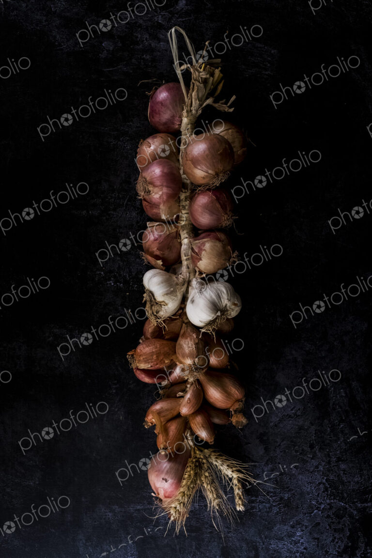 High angle close up of string of onions and garlic on black background.