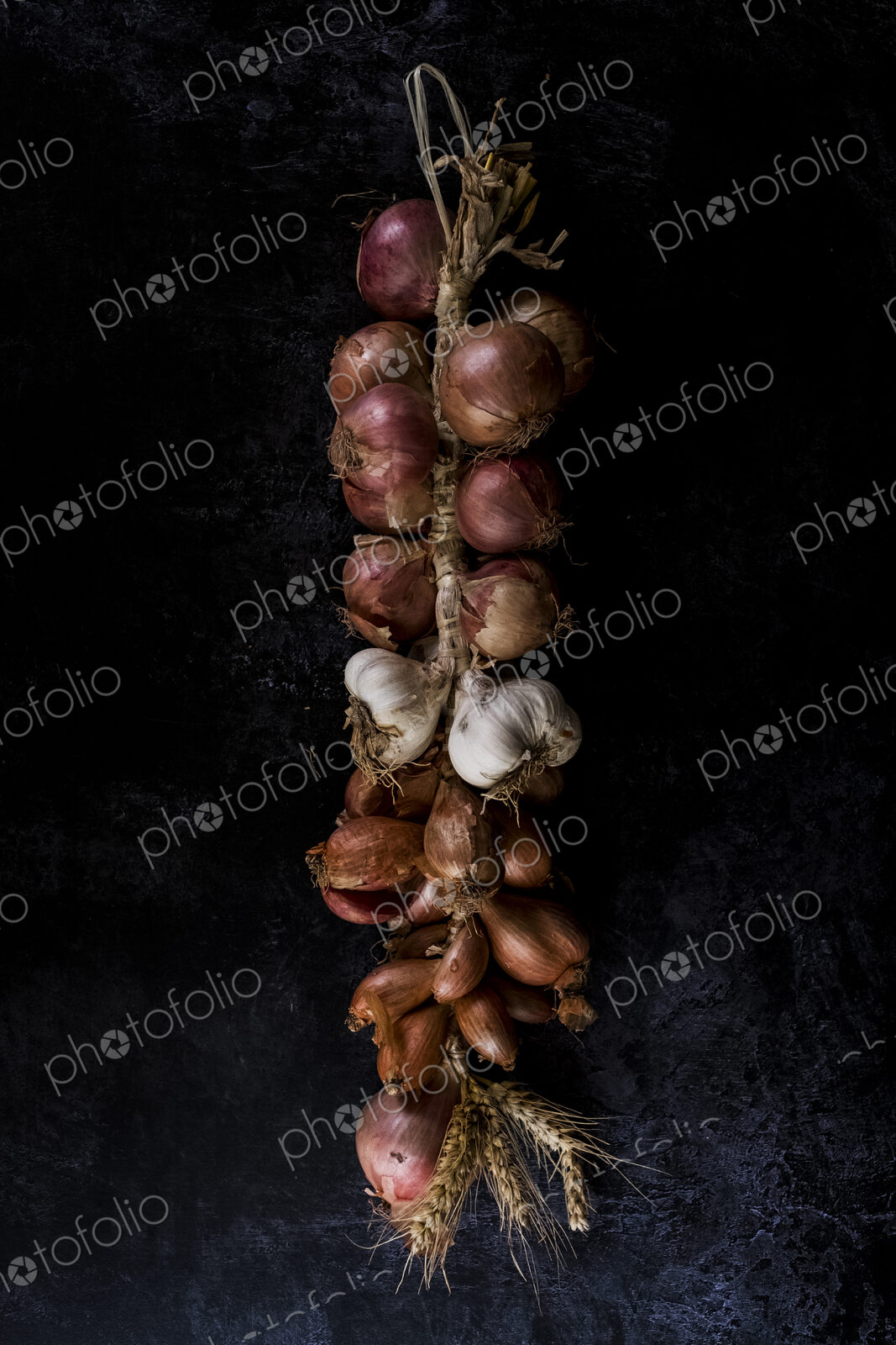 High angle close up of string of onions and garlic on black background.