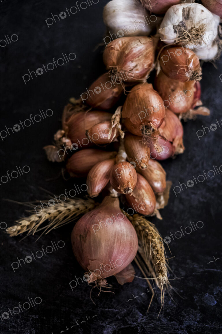 High angle close up of string of onions and garlic on black background.