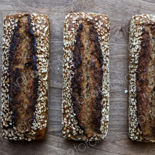 High angle close up of three freshly baked seeded loaves of bread in an artisan bakery.