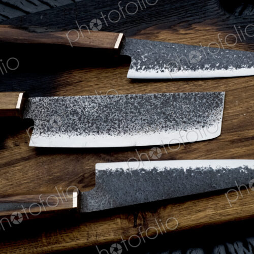 High angle close up of three handmade knives on wooden cutting board. High angle close up of three handmade knives on wooden cutting board.