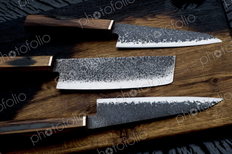 High angle close up of three handmade knives on wooden cutting board.