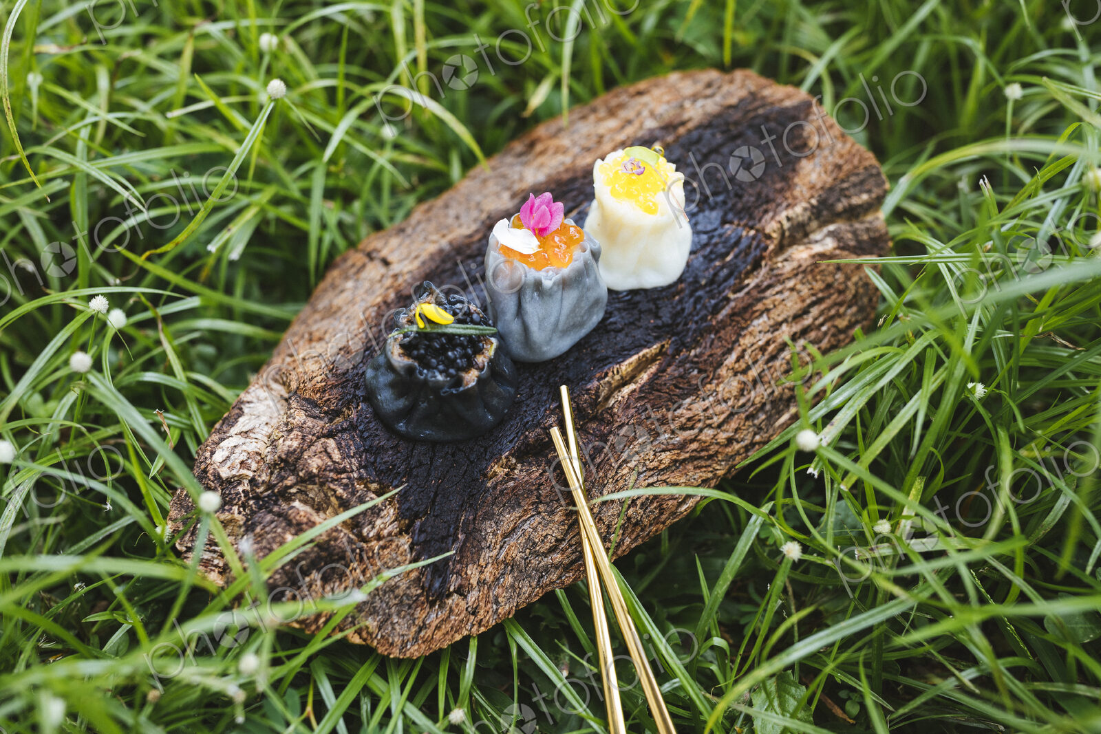 High angle close up of three siew mai dumplings on piece of tree bark on grass.
