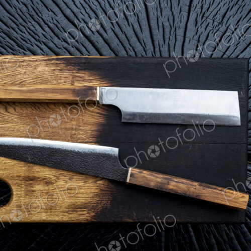 High angle close up of two handmade knives on wooden cutting board. High angle close up of two handmade knives on wooden cutting board.