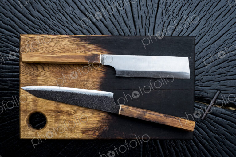 High angle close up of two handmade knives on wooden cutting board.