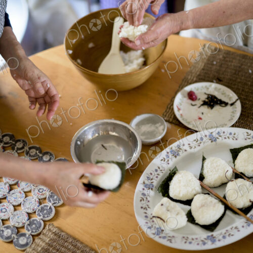 High angle close up of two women standing at a table, preparing plate of sushi.