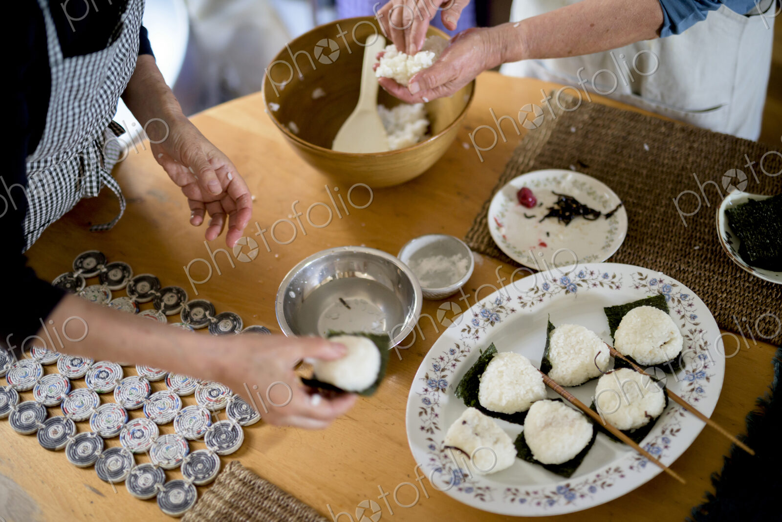 High angle close up of two women standing at a table, preparing plate of sushi.