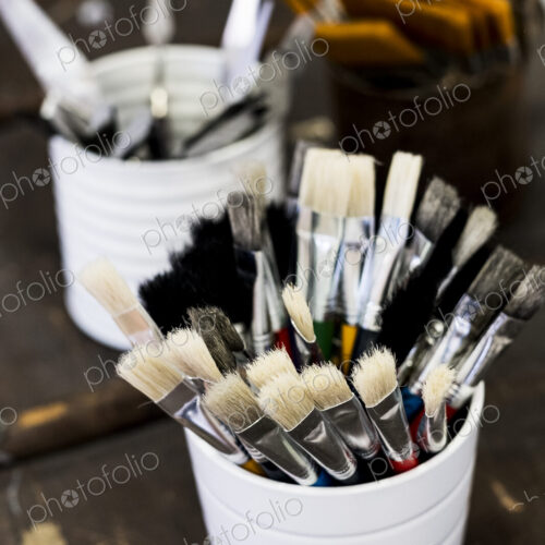 High angle close up of white ceramic pot with selection of paintbrushes in various sizes.