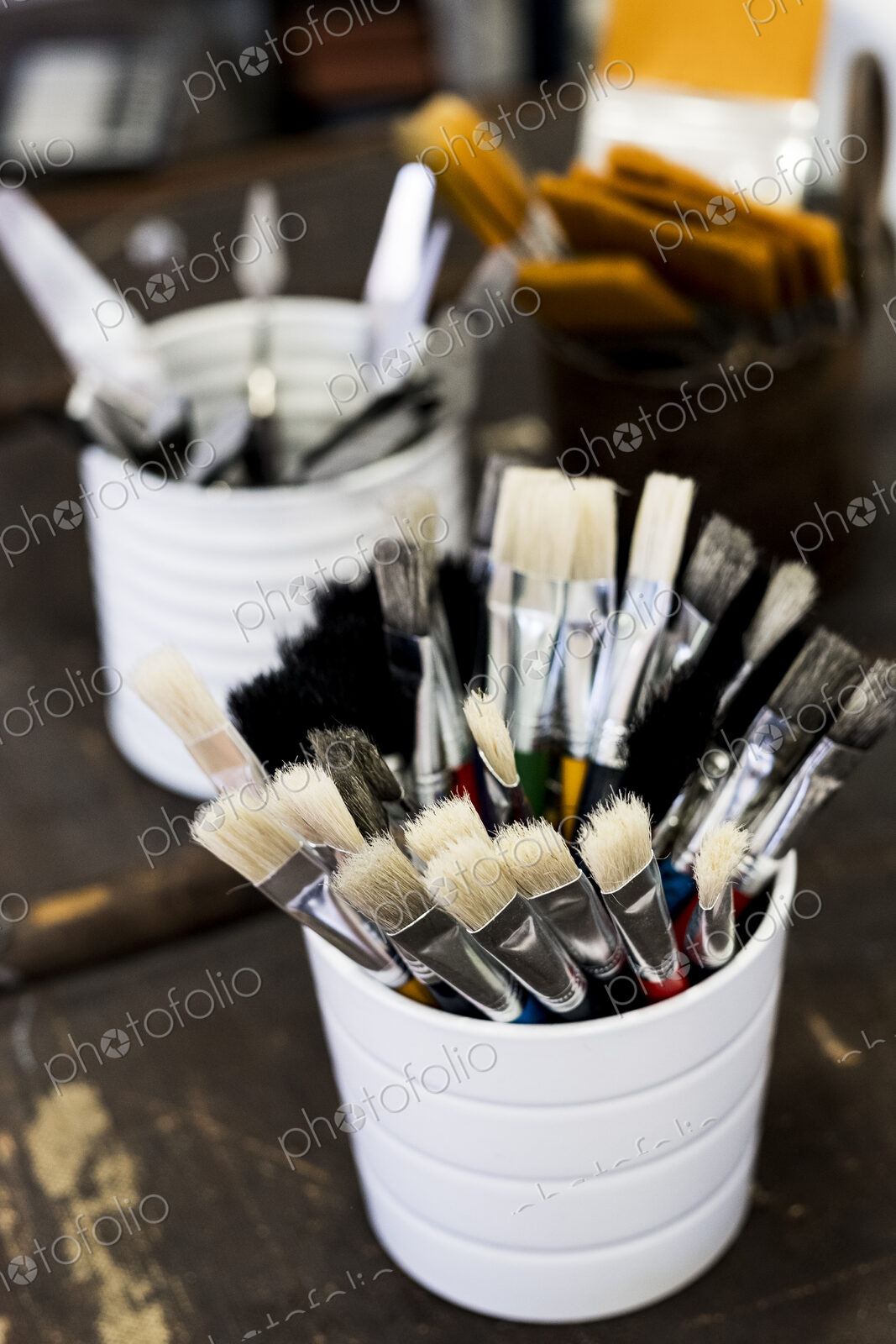 High angle close up of white ceramic pot with selection of paintbrushes in various sizes.