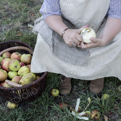 High angle close up of woman sitting in an orchard next to brown wicker basket with…