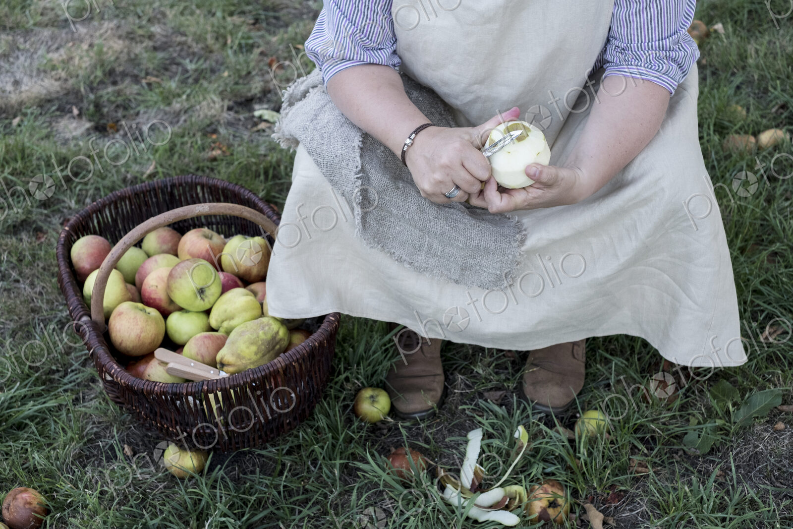 High angle close up of woman sitting in an orchard next to brown wicker basket with…