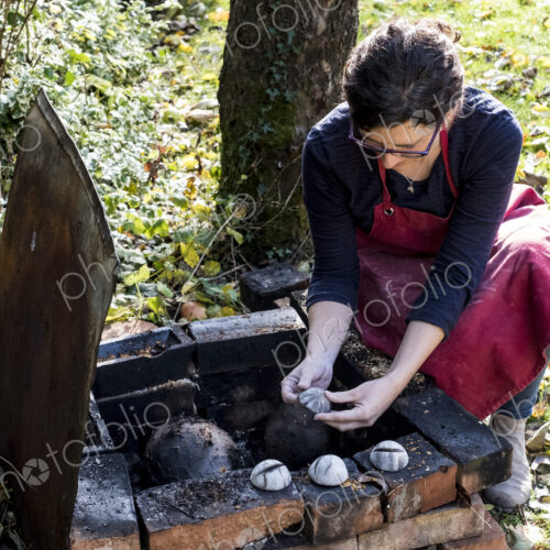 High angle close up of woman wearing red apron kneeling next to outdoor smoke fire…
