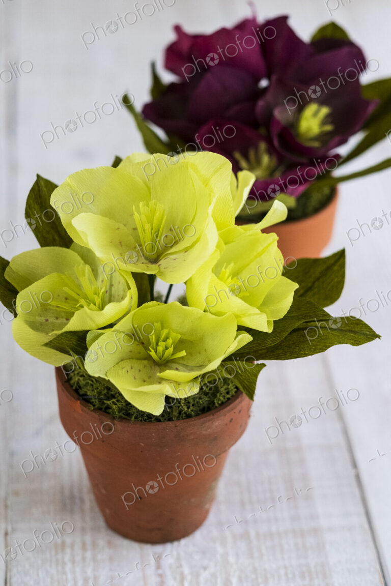 High angle close up of yellow and purple paper flowers in terracotta flowerpots.