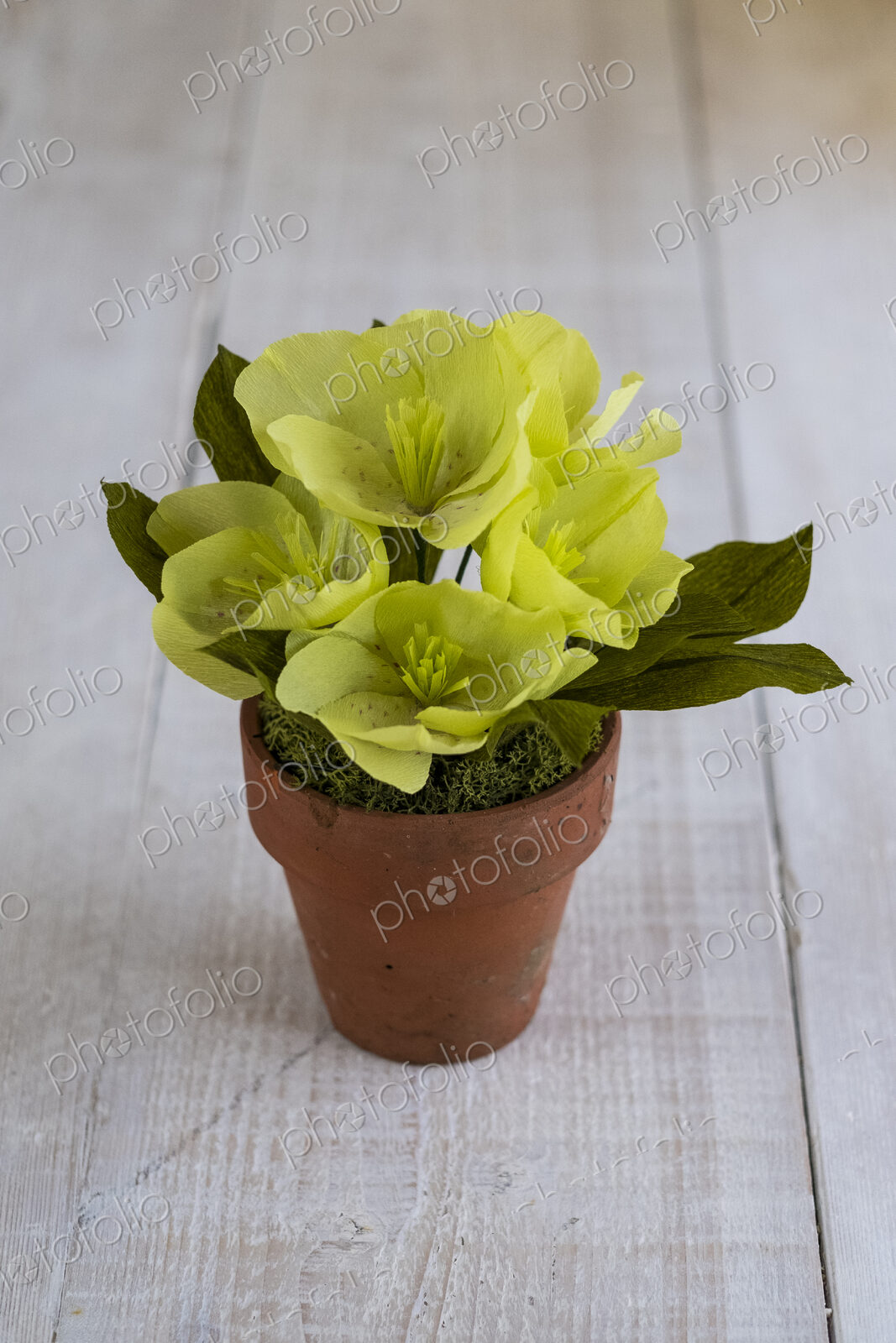 High angle close up of yellow paper flowers in a terracotta flowerpot.