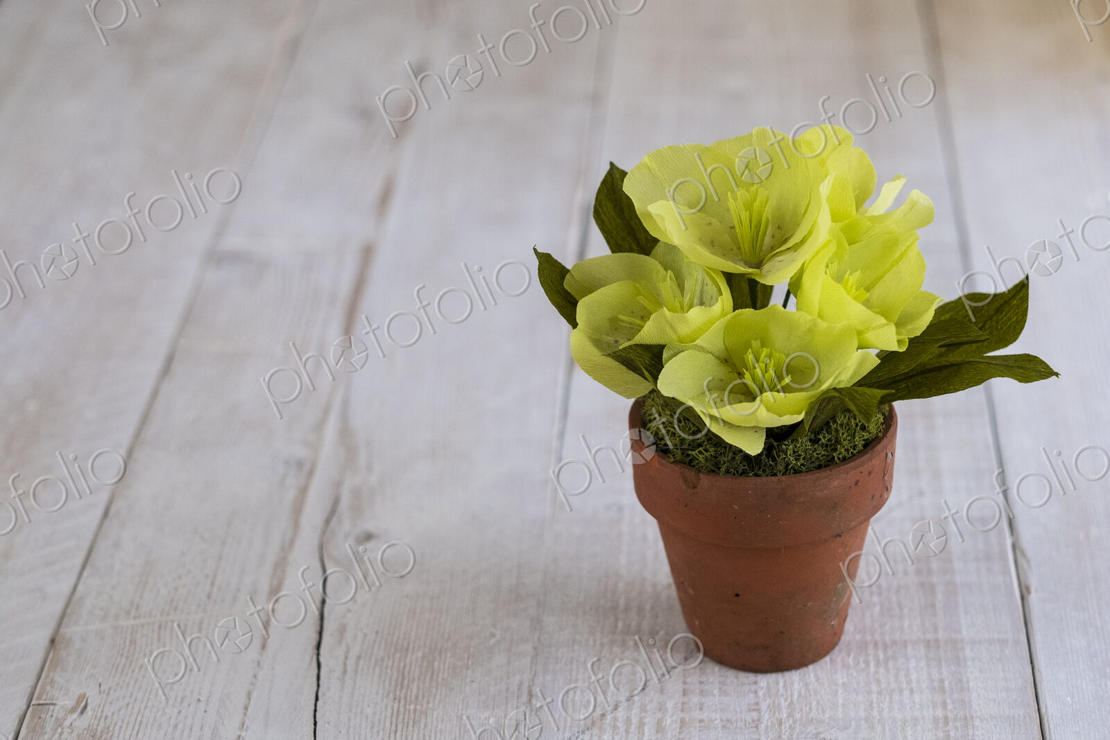 High angle close up of yellow paper flowers in a terracotta flowerpot.