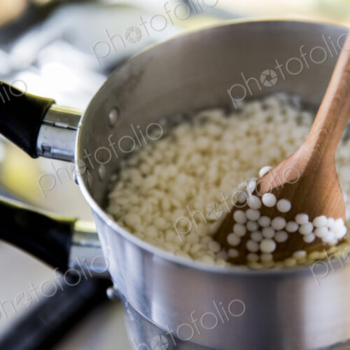 High angle close up wax granules for candles in saucepan on stove.