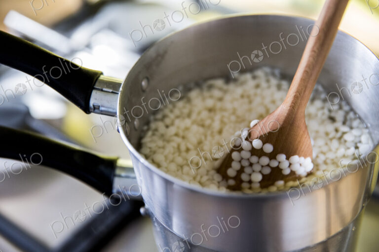 High angle close up wax granules for candles in saucepan on stove.