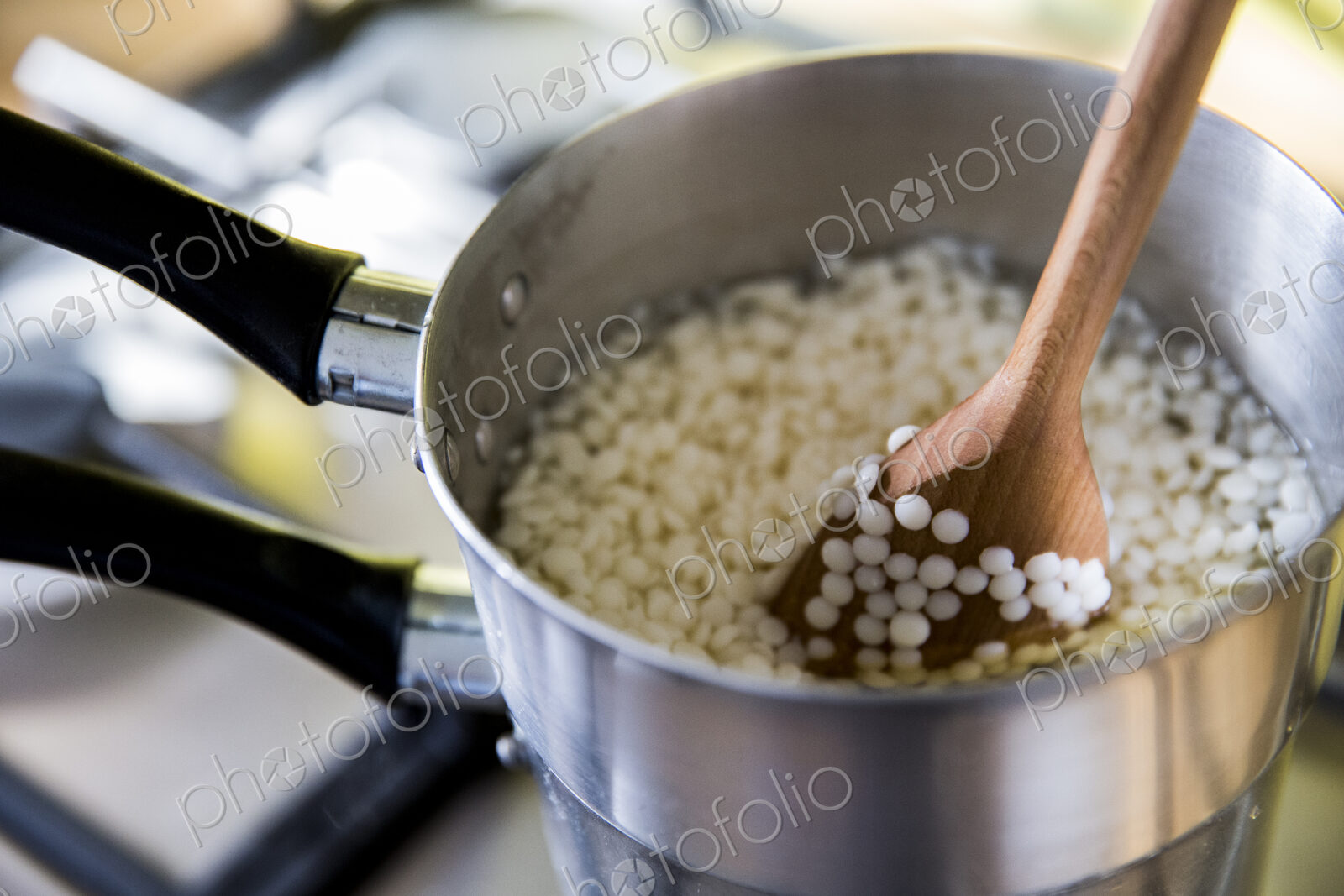 High angle close up wax granules for candles in saucepan on stove.