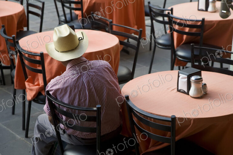 High angle rear view of man wearing Stetson hat sitting a ta a table in a restaurant.