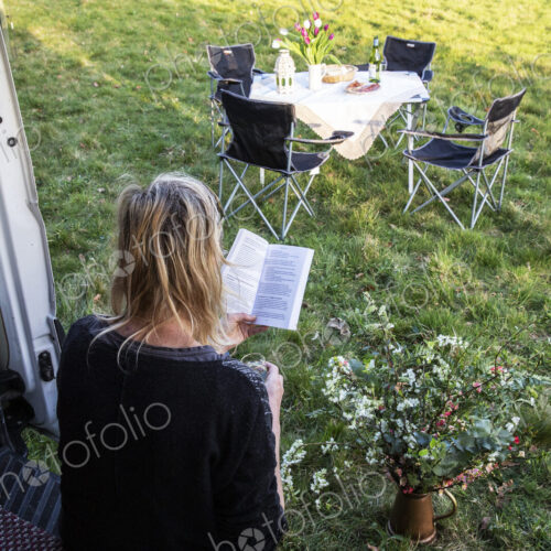 High angle rear view of woman sitting in door of camper van parked on a meadow,…