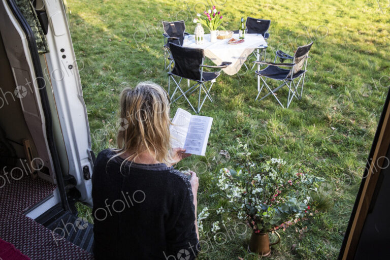 High angle rear view of woman sitting in door of camper van parked on a meadow,…