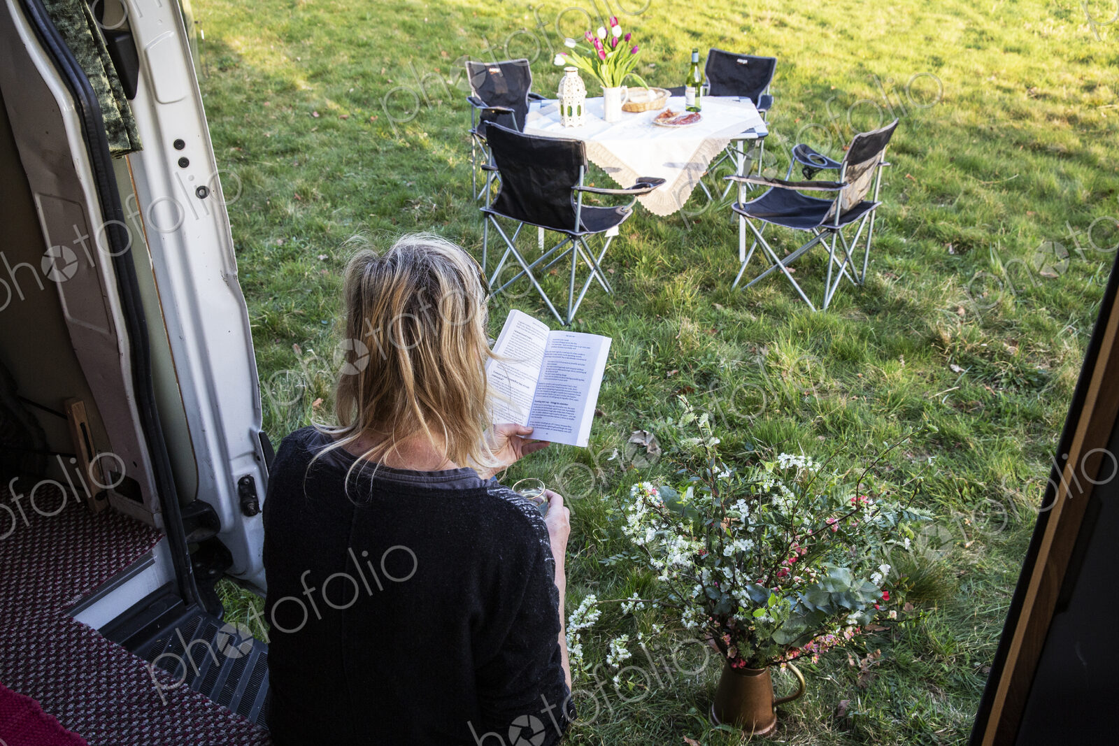 High angle rear view of woman sitting in door of camper van parked on a meadow,…