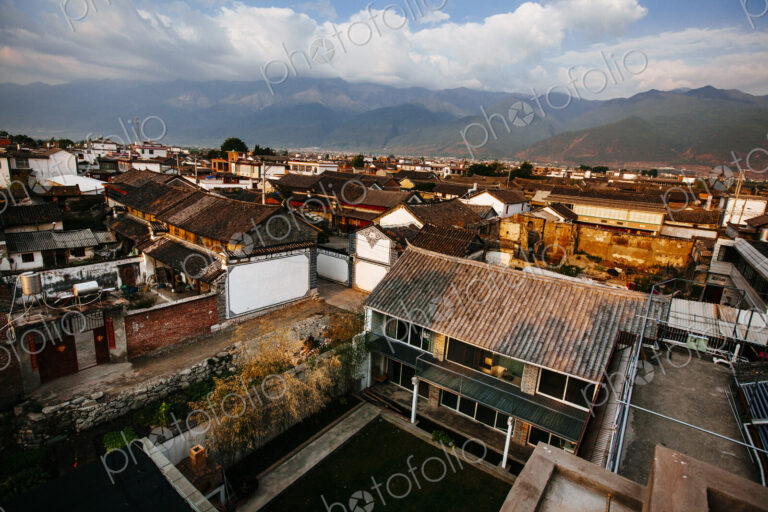 High angle view across rooftops of traditional Asian houses, mountains in the distance.