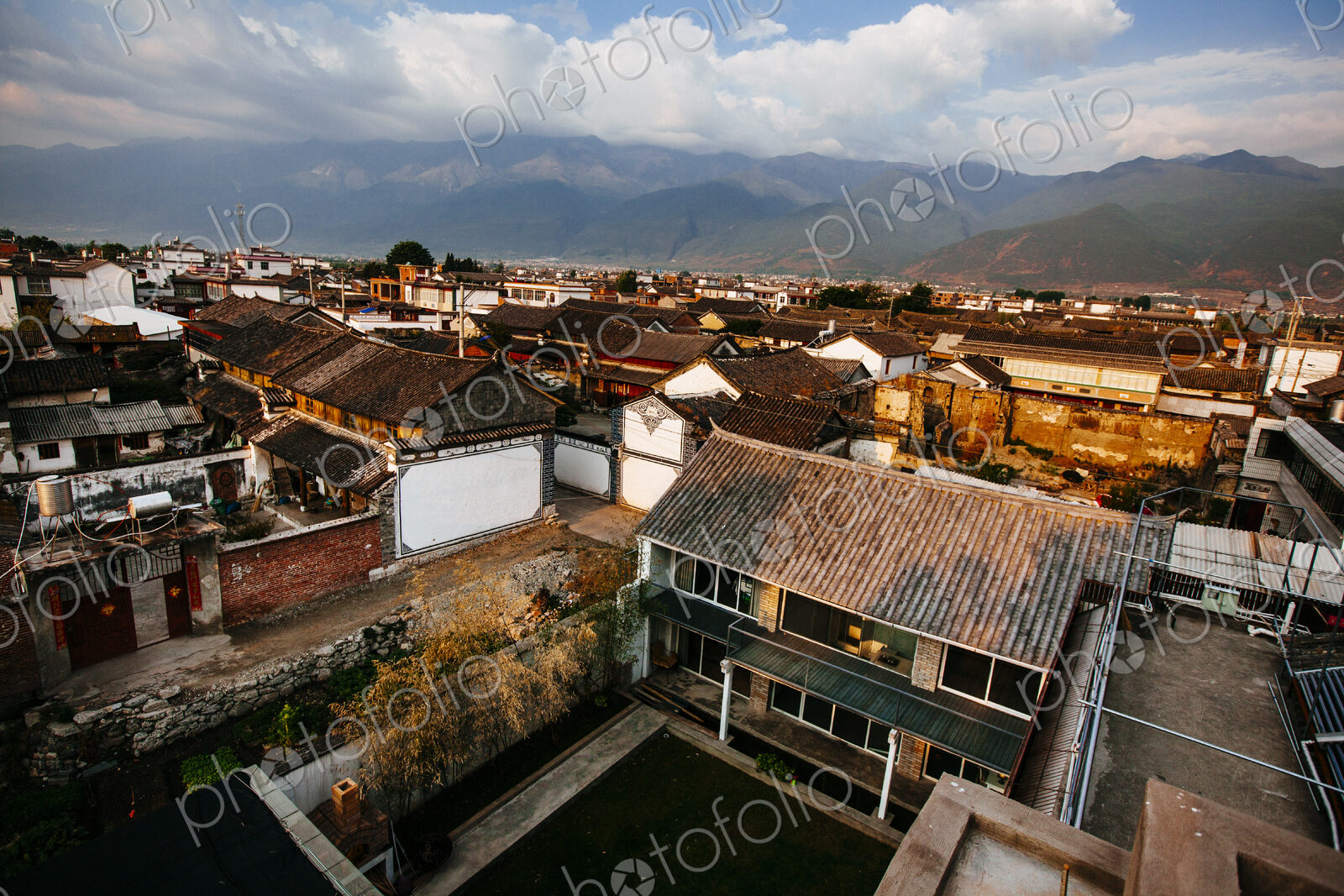 High angle view across rooftops of traditional Asian houses, mountains in the distance.