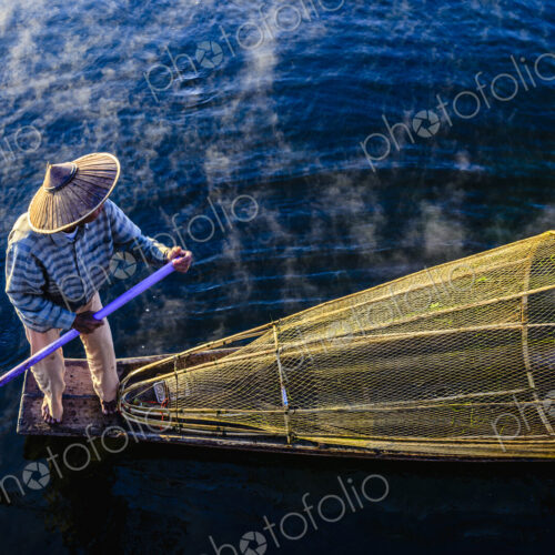 High angle view of Asian fisherman using fishing net in canoe on river