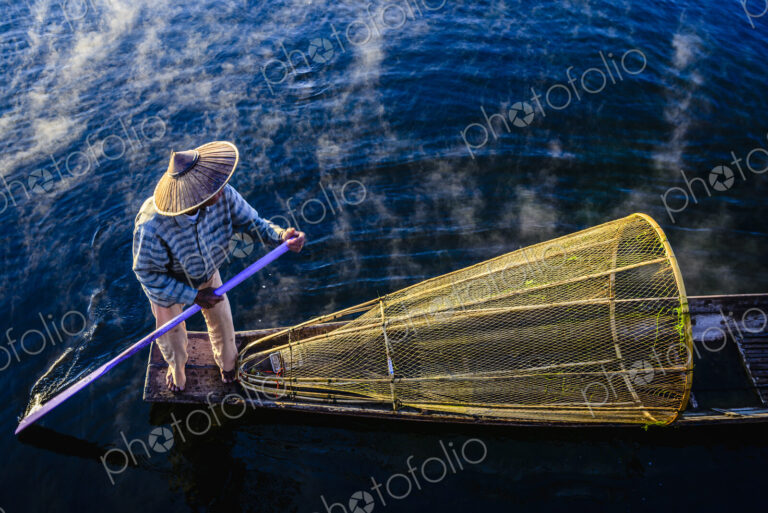 High angle view of Asian fisherman using fishing net in canoe on river