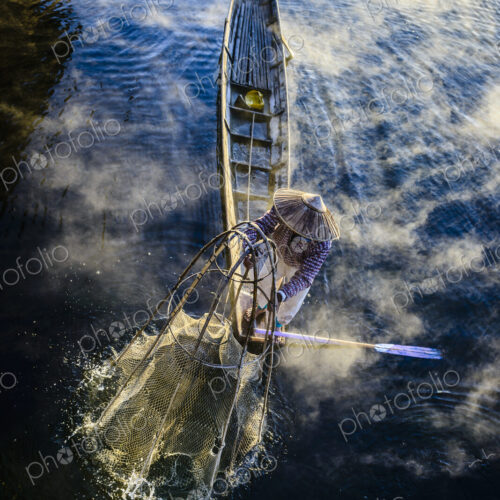 High angle view of Asian fisherman using fishing net in canoe on river