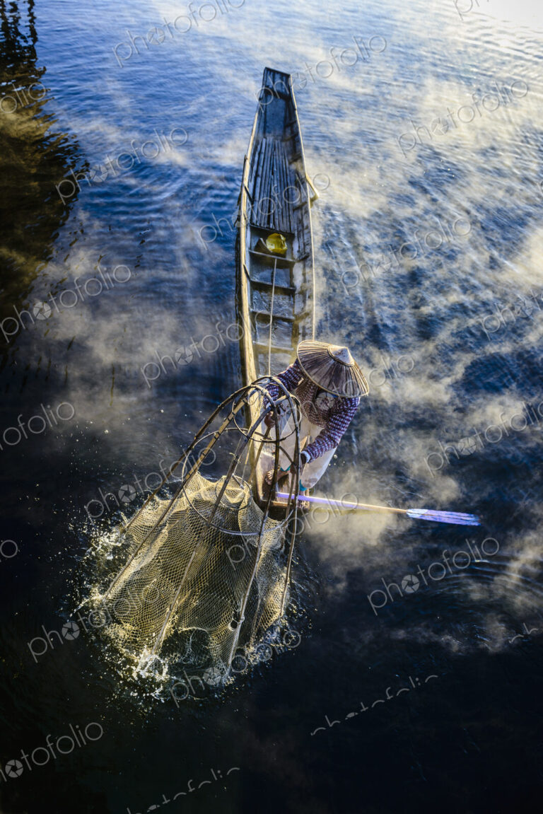 High angle view of Asian fisherman using fishing net in canoe on river